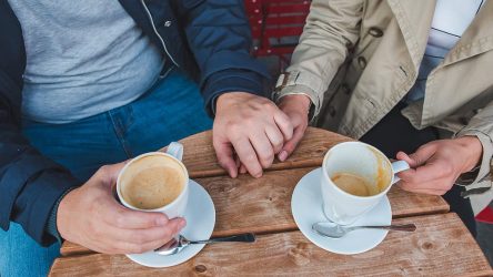 couple-holding-hands-while-drinking-latte-outdoors-cafe