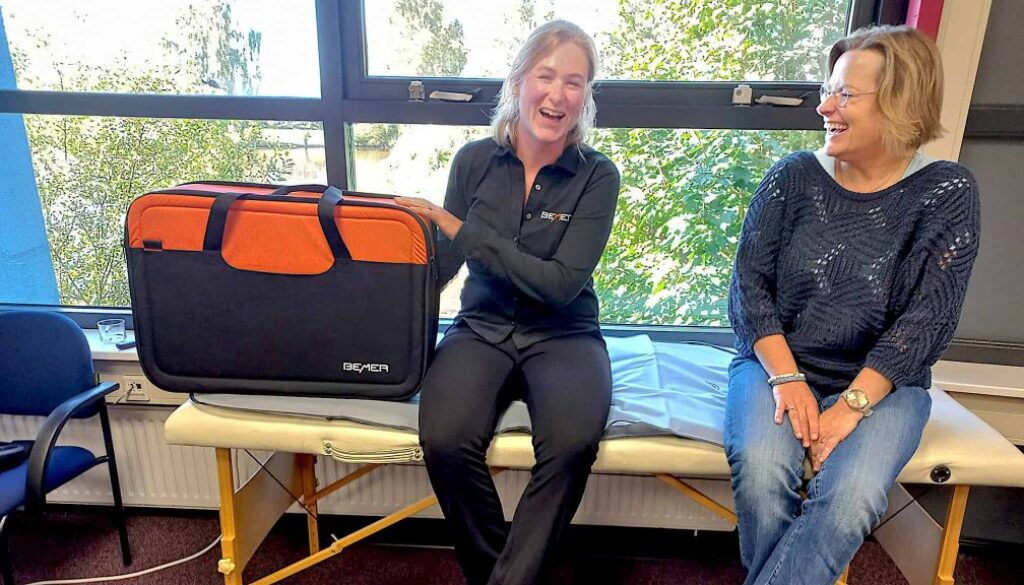 Grote zwarte en oranje medische tas met logo van Bemil, lachende verpleegkundige en patiënt tijdens een consult in het ziekenhuis.
