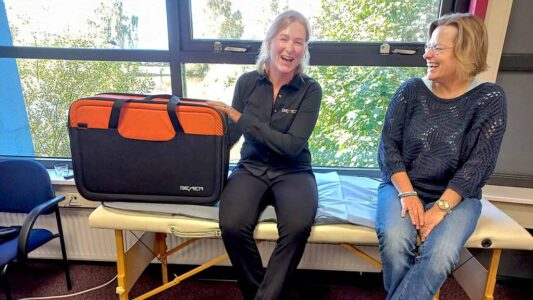 Grote zwarte en oranje medische tas met logo van Bemil, lachende verpleegkundige en patiënt tijdens een consult in het ziekenhuis.