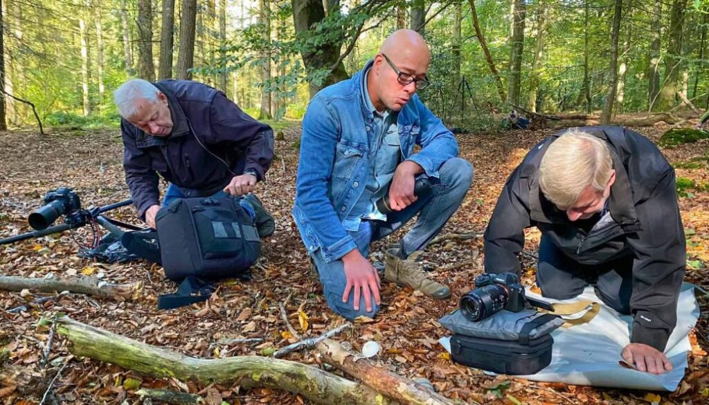 Fotografie van drie mensen die in een bos onderzoek doen naar natuur en biodiversiteit, met professionele uitrusting en camera's voor natuurfotografie en wildlife observation, organisch en natuurlijk achtergrondbeeld.
