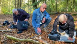 Fotografie van drie mensen die in een bos onderzoek doen naar natuur en biodiversiteit, met professionele uitrusting en camera's voor natuurfotografie en wildlife observation, organisch en natuurlijk achtergrondbeeld.