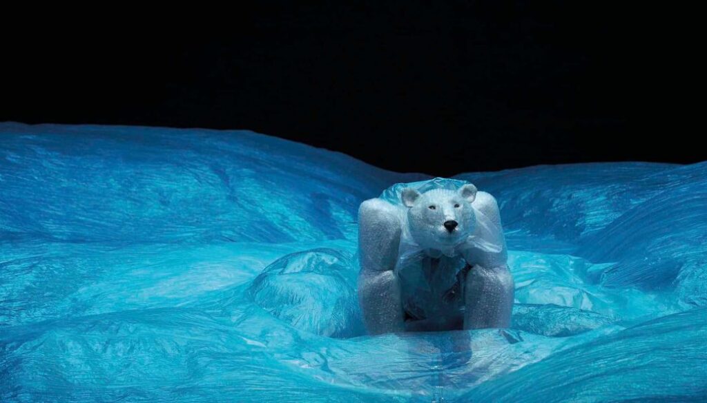 Robuuste ijsbeerfiguur op ijslandschap, gemaakt van kunstmatig ijs en plastic, afgebeeld bij nacht met helder blauw ijs en donkere lucht, symbool voor natuurbescherming en kunstprojecten.