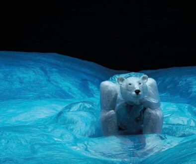 Robuuste ijsbeerfiguur op ijslandschap, gemaakt van kunstmatig ijs en plastic, afgebeeld bij nacht met helder blauw ijs en donkere lucht, symbool voor natuurbescherming en kunstprojecten.