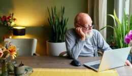Knusse woonkamer met oudere man workend op laptop, omringd door groene planten, bloemen en sfeervol licht, perfect voor een gezellige en rustgevende sfeer.