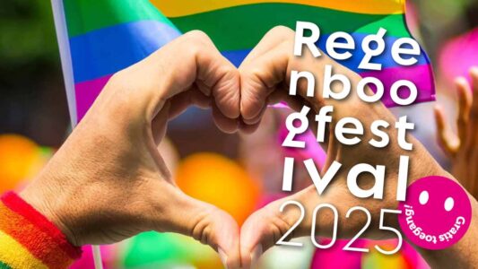 Kleurrijke handen vormen een hart tijdens het LGBT+ Pride Festival 2025 met regenboogvlag in de achtergrond.