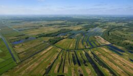 Luchtfoto van de uitgestrekte waterrijke landbouwgebieden in de omgeving van RTV SLOS, met diverse weilanden, sloten en irrigatiekanalen in een weids landschap.