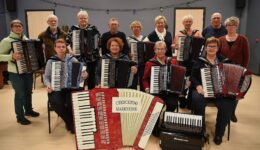Koorleden van RTV SLOS met accordions, samen in een oefenruimte, klaar voor een optreden of repetitie. Muzikanten van verschillende leeftijden spelen een inspirerende en muzikale rol binnen de gemeenschap.