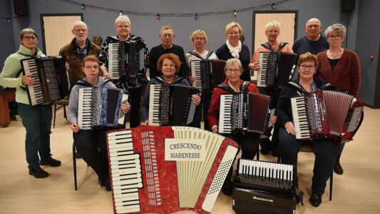 Koorleden van RTV SLOS met accordions, samen in een oefenruimte, klaar voor een optreden of repetitie. Muzikanten van verschillende leeftijden spelen een inspirerende en muzikale rol binnen de gemeenschap.