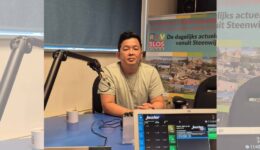 RTV SLOS presentator tijdens interview in radiostudio met RTV SLOS banner op achtergrond.