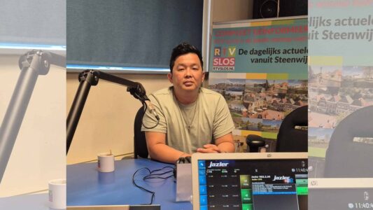 RTV SLOS presentator tijdens interview in radiostudio met RTV SLOS banner op achtergrond.