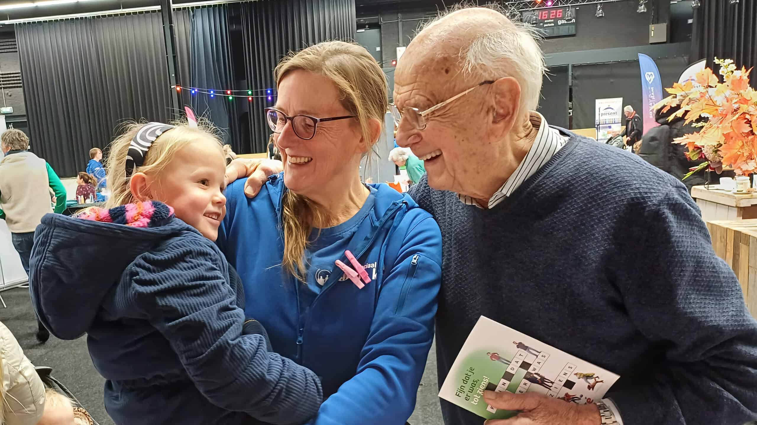 Vriendelijke jonge meid met ouder en grootouder die samen lachen, in een gezellige indoor evenement setting met kleurrijke decoraties, verbondenheid en familiewaarden, gericht op gemeenschap en cultuur, voor optimale SEO.