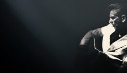 Gitarist in zwarte en witte jas met snaren, zwart-wit foto, muziek, entertainment, RTV SLOS.