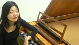 Mooie jonge vrouw die piano speelt op een houten klavecimbel in een sfeervolle muzikale setting.