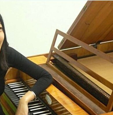 Mooie jonge vrouw die piano speelt op een houten klavecimbel in een sfeervolle muzikale setting.