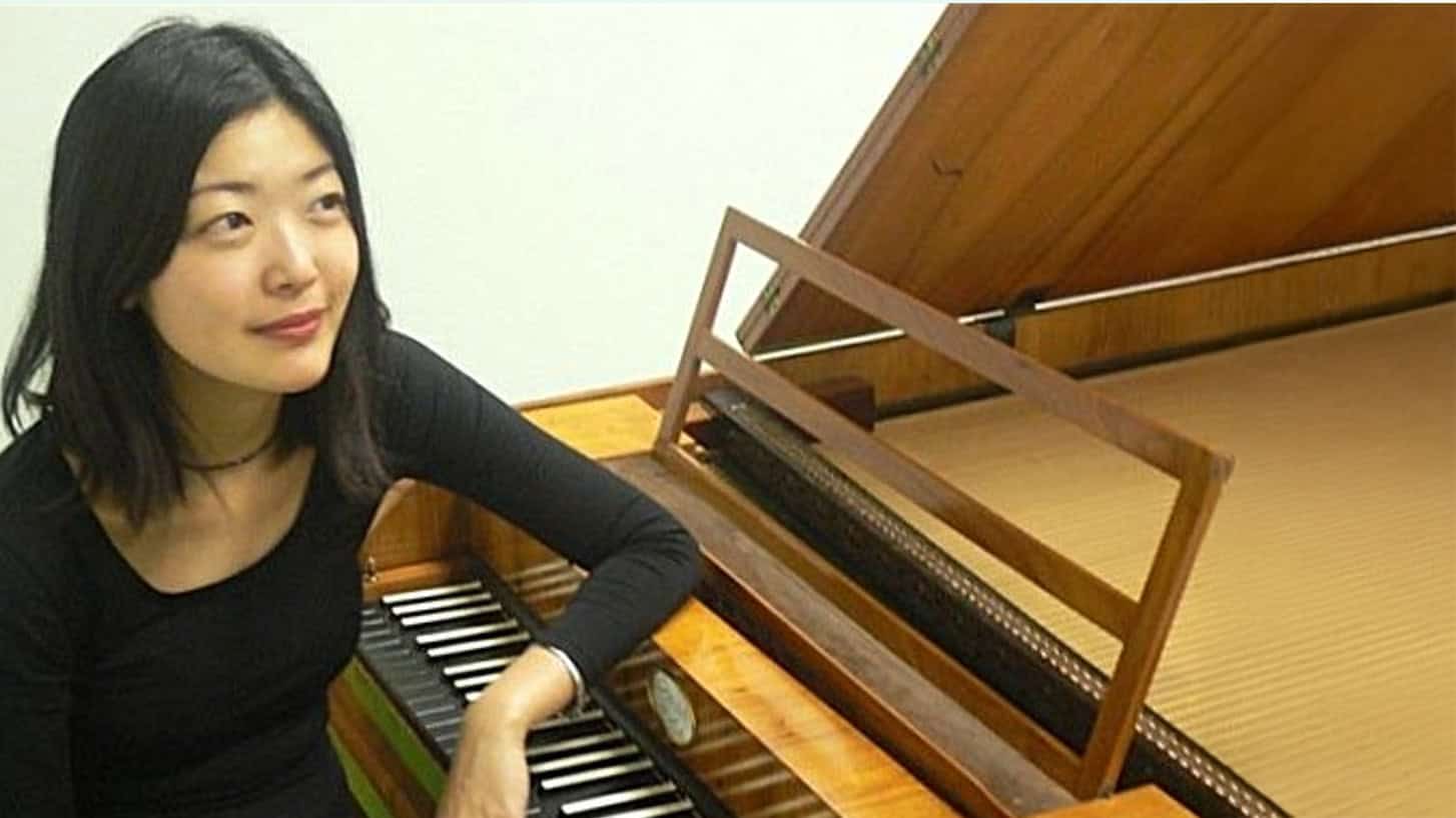 Mooie jonge vrouw die piano speelt op een houten klavecimbel in een sfeervolle muzikale setting.