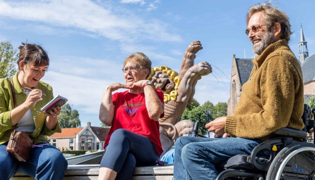 Vrolijke mensen in gesprek op een plein met beelden en een kerk op de achtergrond, glimlachend en genietend van een zonnige dag, benadrukt inclusieve gemeenschap en maatschappelijke betrokkenheid.