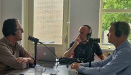 Man die in microfoon spreekt tijdens radio-opname bij RTV SLOS, podcast opname, radiostudio met drie mensen met koptelefoons, gesprek over lokale media en community nieuws in Nederland.