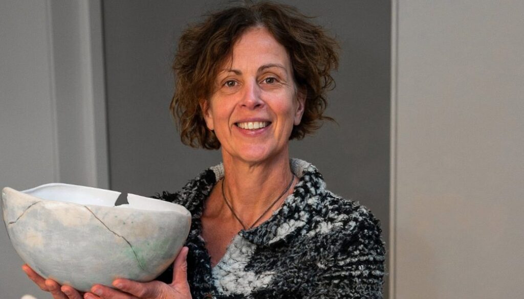Vrouw met kort, golvend haar toont een keramische kunstwerk waarin ze glimlachend haar kunstverhaal deelt. RTV SLOS biedt achtergrondinformatie over haar creatieve keramiek en artistieke passie.