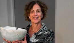 Vrouw met kort, golvend haar toont een keramische kunstwerk waarin ze glimlachend haar kunstverhaal deelt. RTV SLOS biedt achtergrondinformatie over haar creatieve keramiek en artistieke passie.