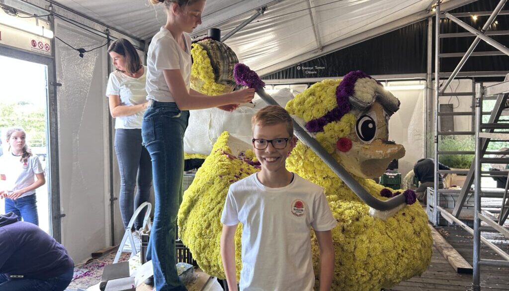 Jonge corsobouwers prikken gele dahlia’s op de juniorcorsowagen van Kolonie Junior in Frederiksoord.