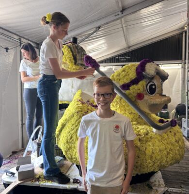 Jonge corsobouwers prikken gele dahlia’s op de juniorcorsowagen van Kolonie Junior in Frederiksoord.