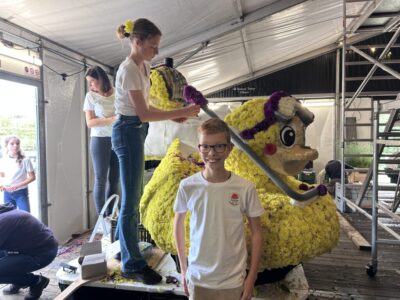 Jonge corsobouwers prikken gele dahlia’s op de juniorcorsowagen van Kolonie Junior in Frederiksoord.